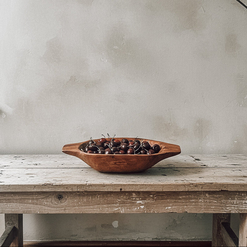 Wooden bowl with fruits on a rustic wooden table against a textured wall.