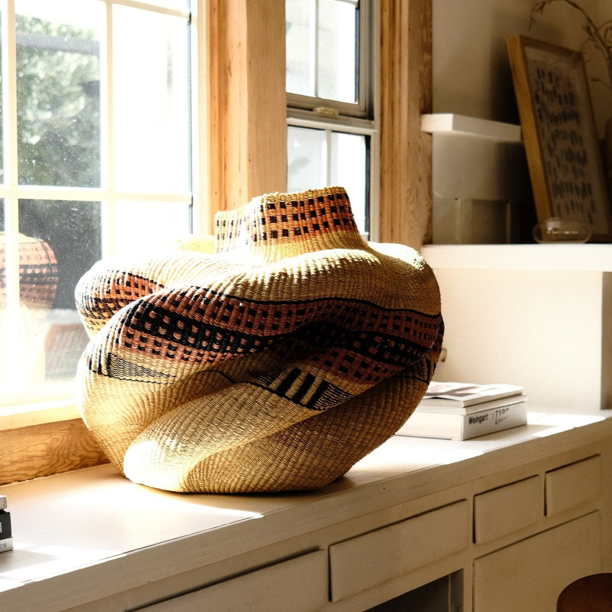 A woven Bolga basket displayed on a white surface with natural lighting from a window in the background.